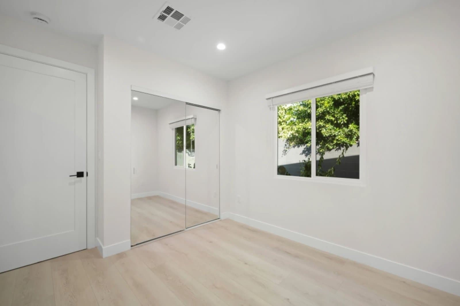 ADU bedroom with mirrored closet doors and garden view