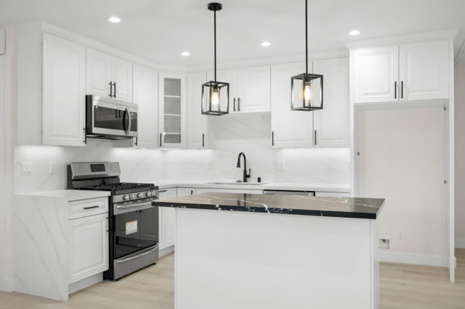 Finished ADU kitchen with white cabinets, black marble island and lantern pendants